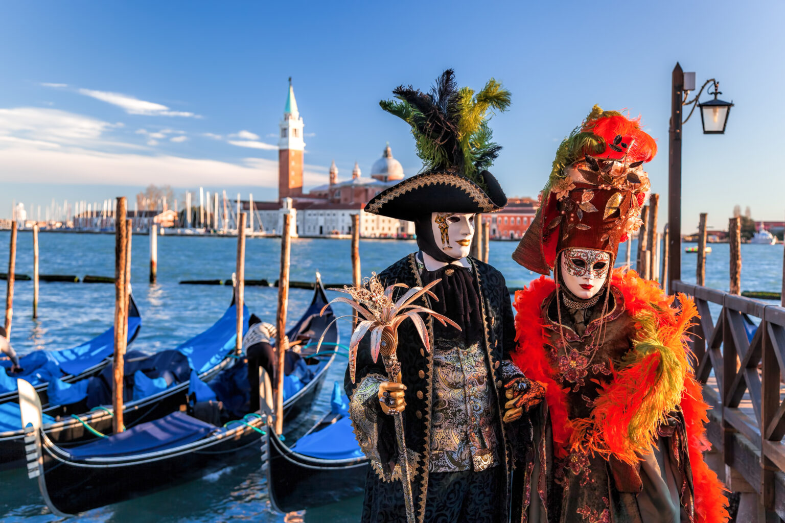 Masked couples in traditional costumes at the Venice Carnival beside gondolas